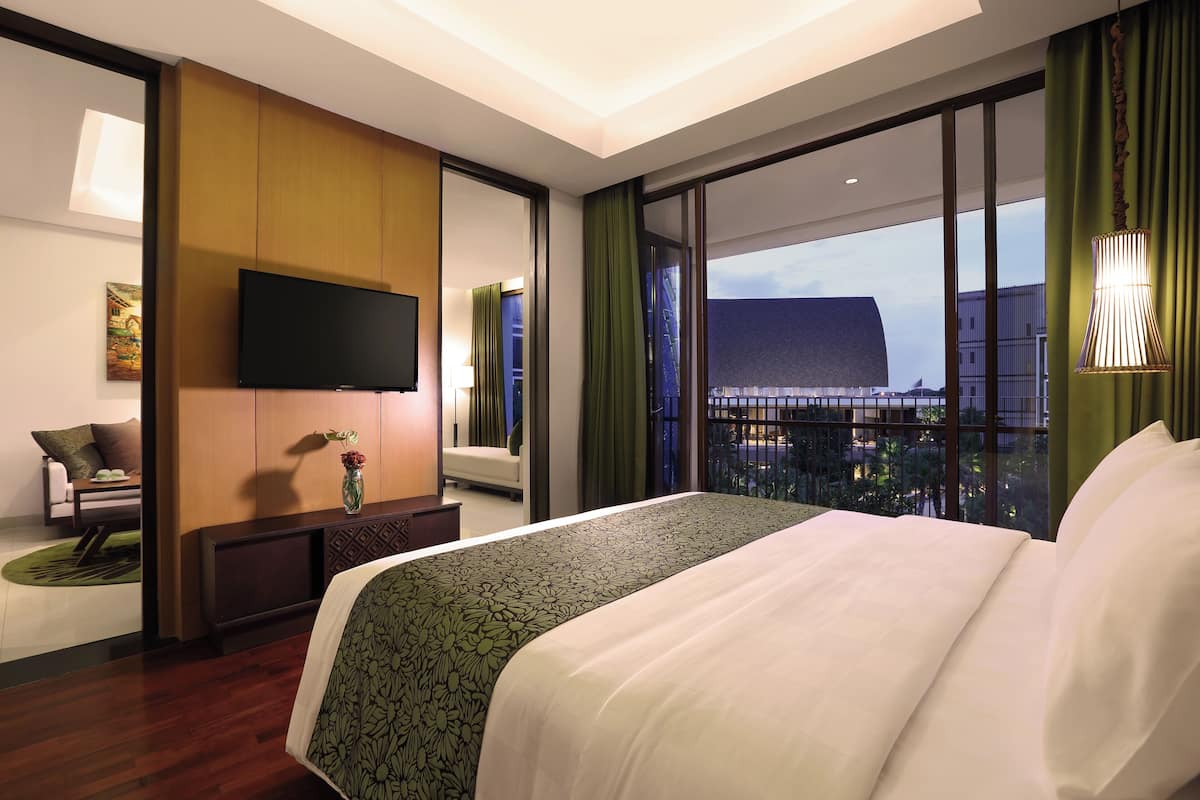 Ein Hotelzimmer mit einem großen Bett, einem Flachbildfernseher, einer Sitzecke und Blick auf die Stadt durch große Fenster.