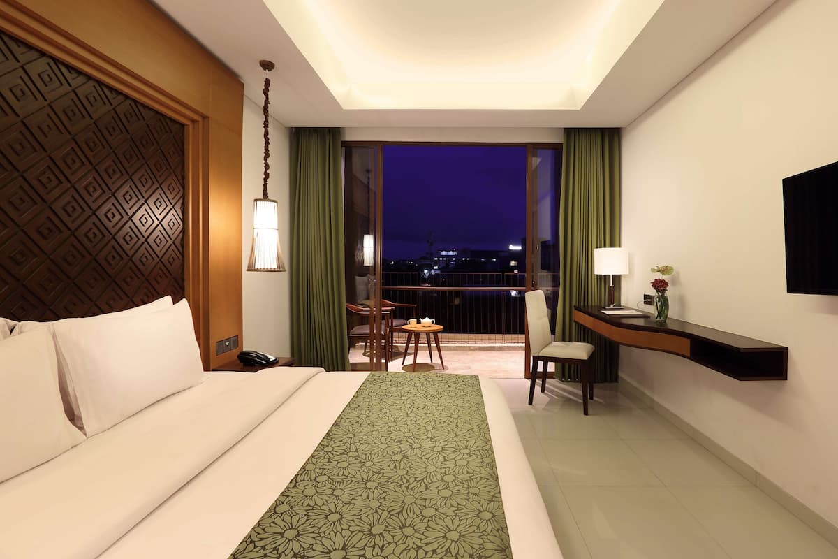Ein Hotelzimmer mit einem großen Bett, einem Schreibtisch, einem Sessel, einem kleinen Tisch und Blick auf die nächtliche Stadt.