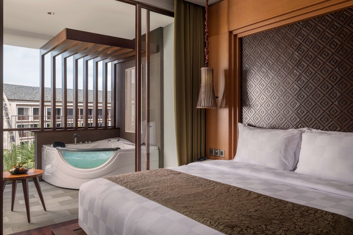 Une chambre d’hôtel avec un grand lit, une baignoire et un balcon donnant sur les bâtiments.