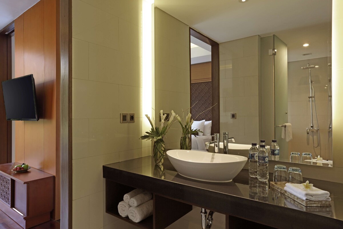 Une salle de bain moderne avec un grand lavabo, un miroir et une douche. On y trouve des serviettes et des articles de toilette sur le comptoir.