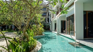 A swimming pool surrounded by lush greenery and modern buildings. - Golden Tulip Jineng Resort Bali (Kuta)