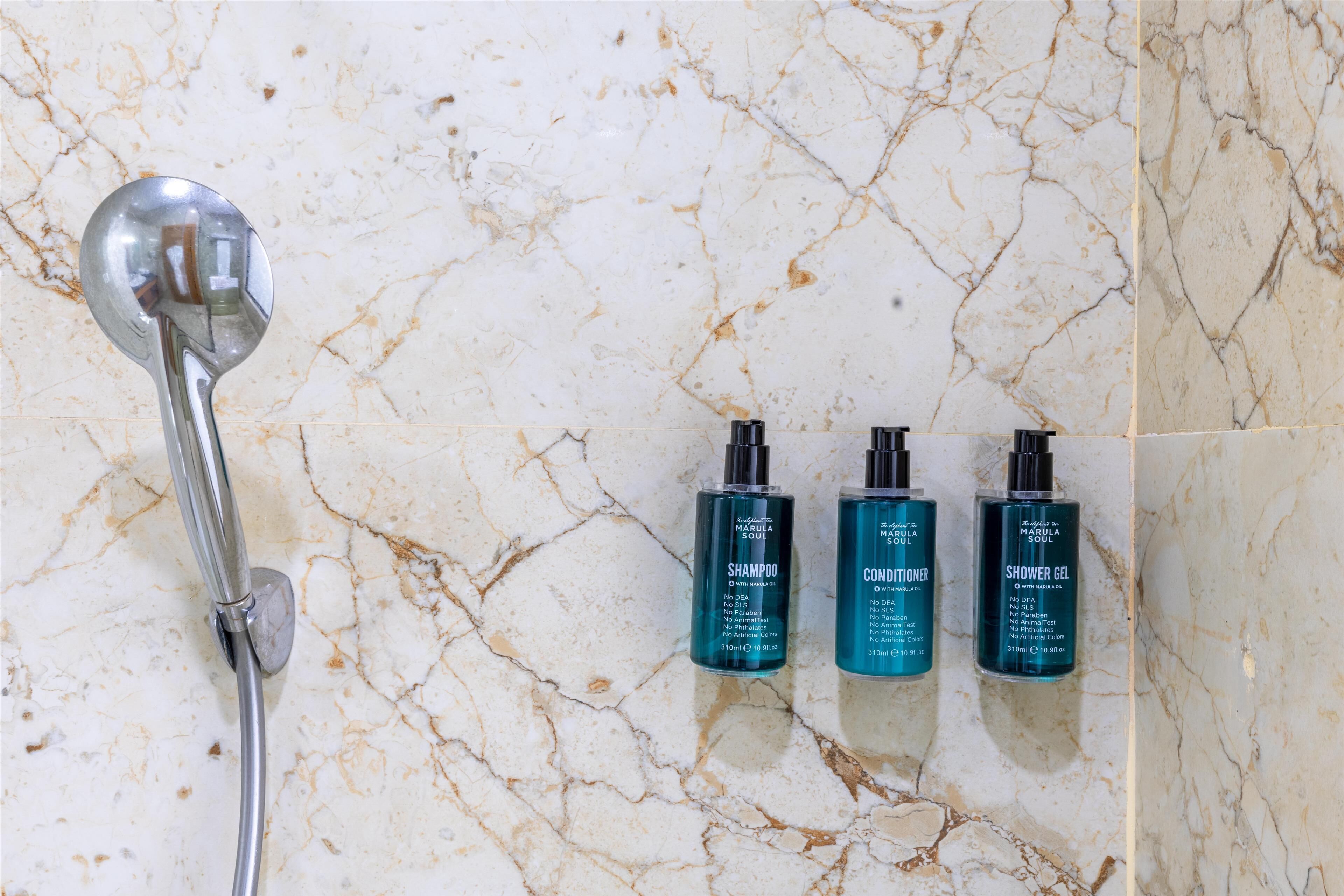 A bathroom with a marble floor, a showerhead, and three bottles of Marula Soul products.
