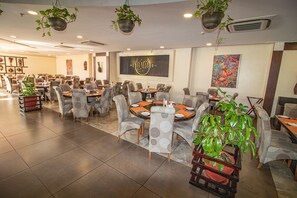 A restaurant with multiple dining tables and chairs, potted plants, and artwork on the walls.