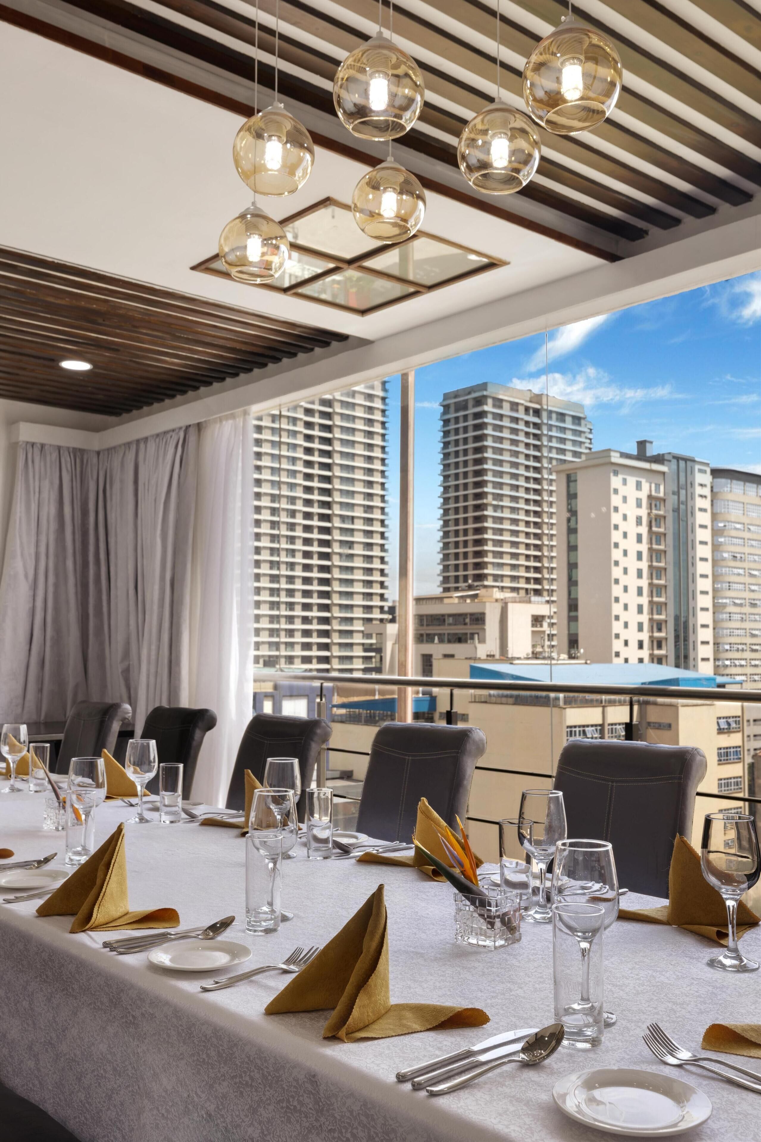 A dining area with a table set for six, large windows, and a cityscape view.