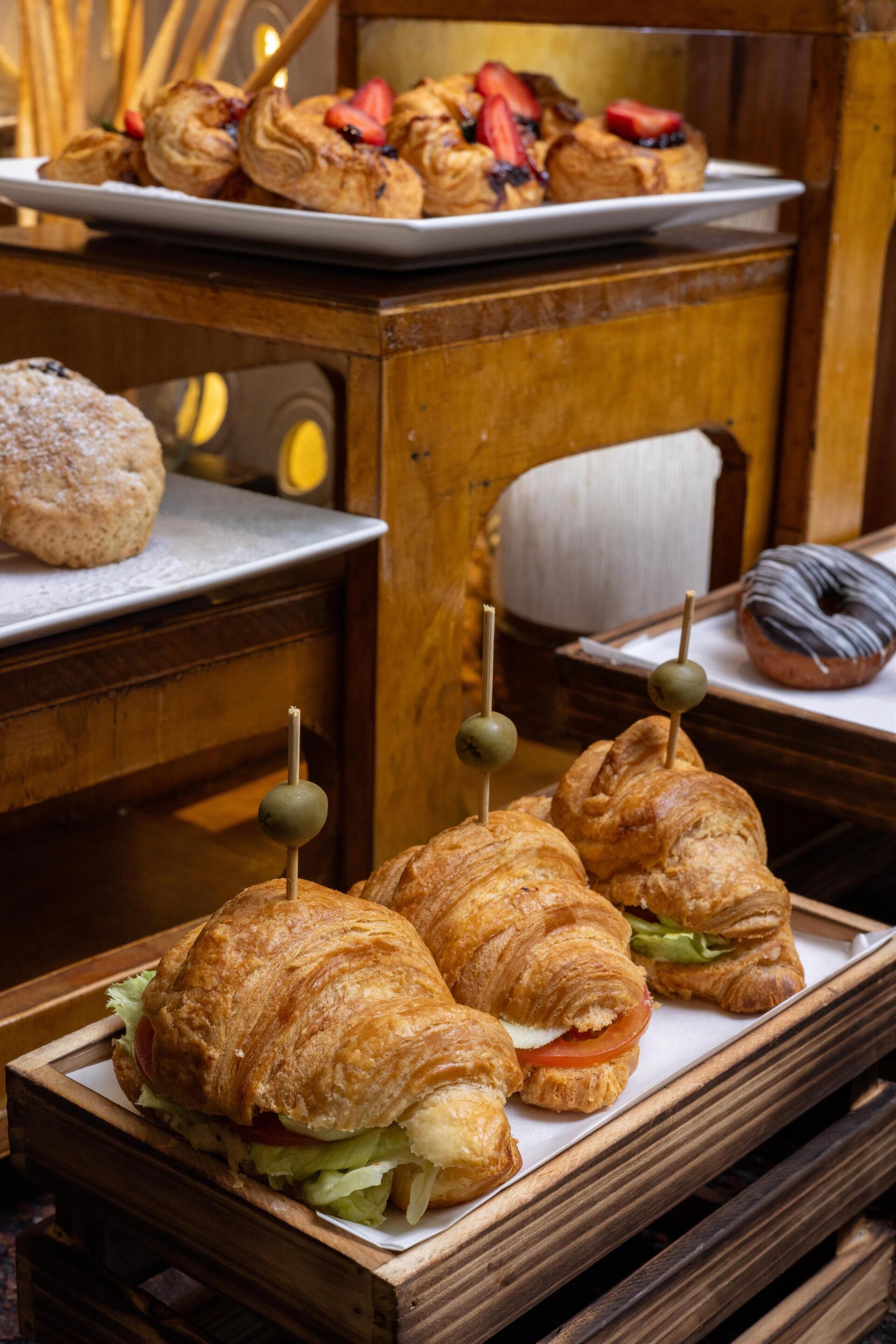 A wooden table with a tray of croissants and sandwiches, a doughnut, and a biscuit.