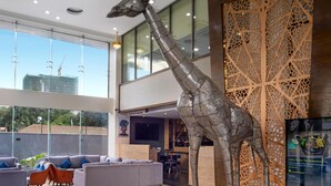 Eine moderne Lobby mit einer großen Giraffenskulptur, einer Chandelüster und Blick auf eine Baustelle.