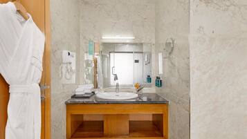 A bathroom with a marble wall, a wooden vanity, a sink, a mirror, and a towel rack.