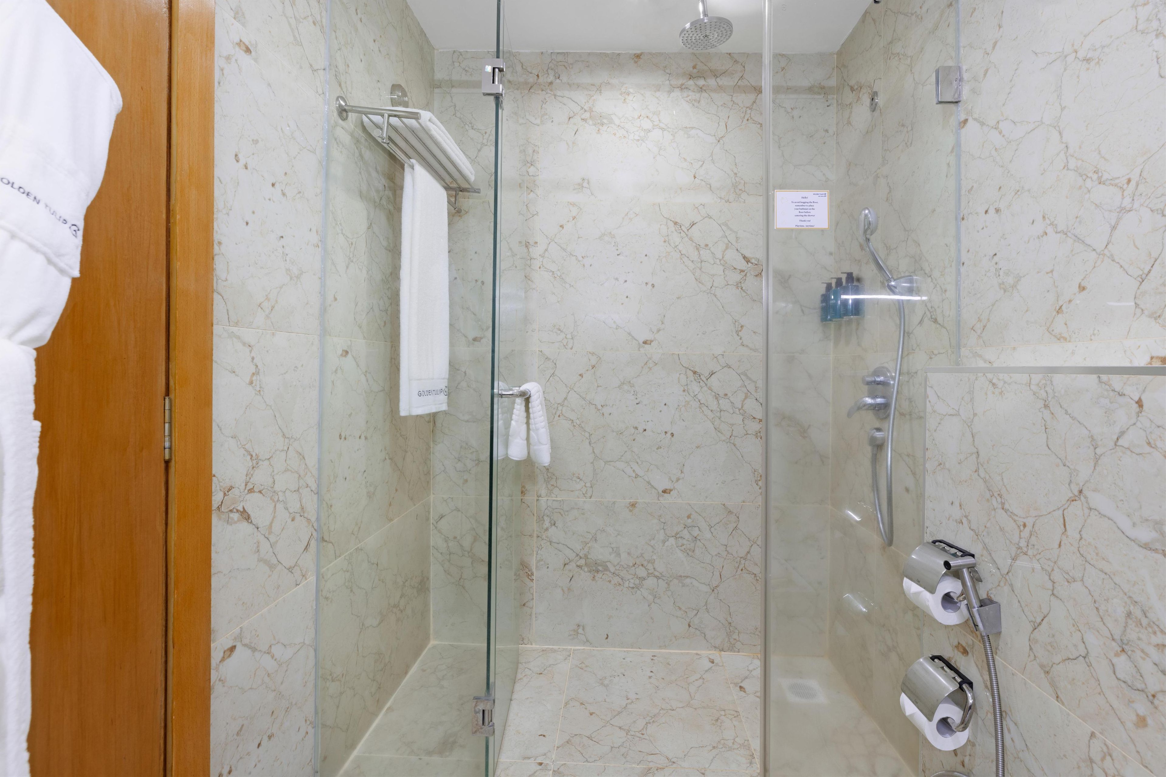 Cabina de ducha con paredes de mármol, un perchero y un cabezal de ducha.