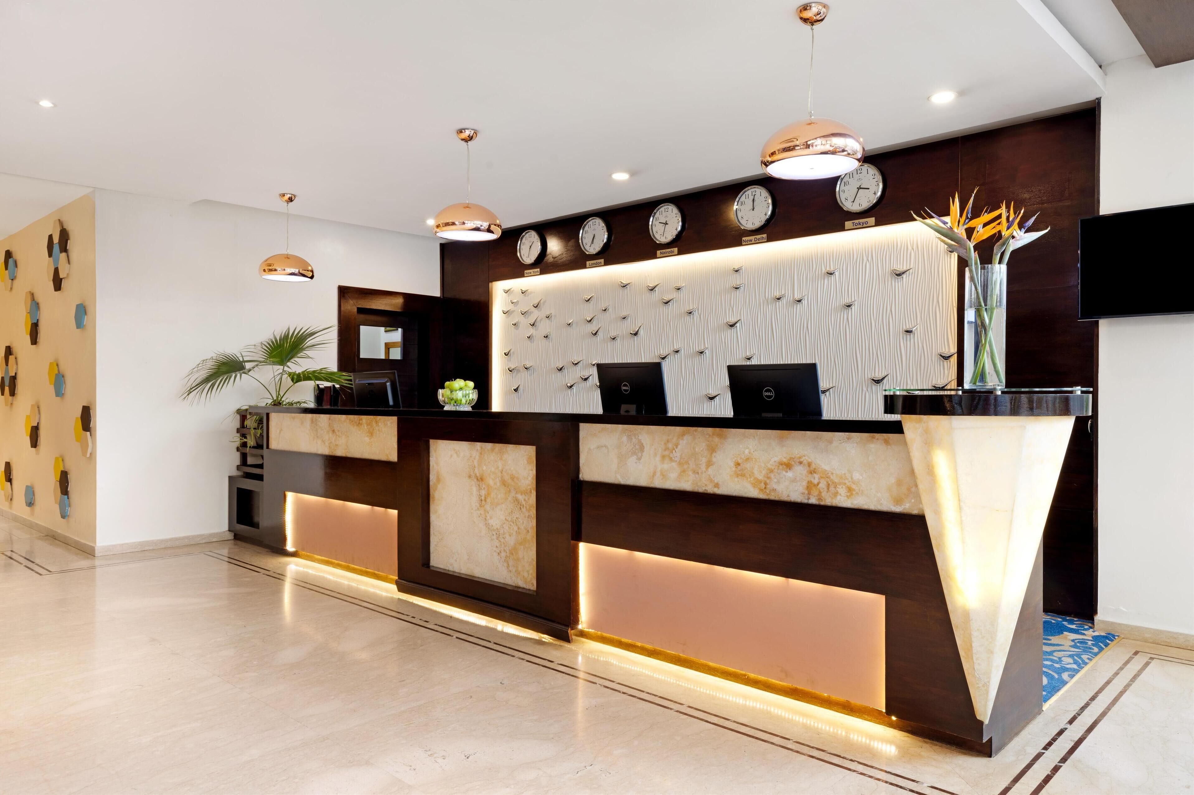 A modern reception desk with integrated clocks, a digital screen, and a decorative plant.