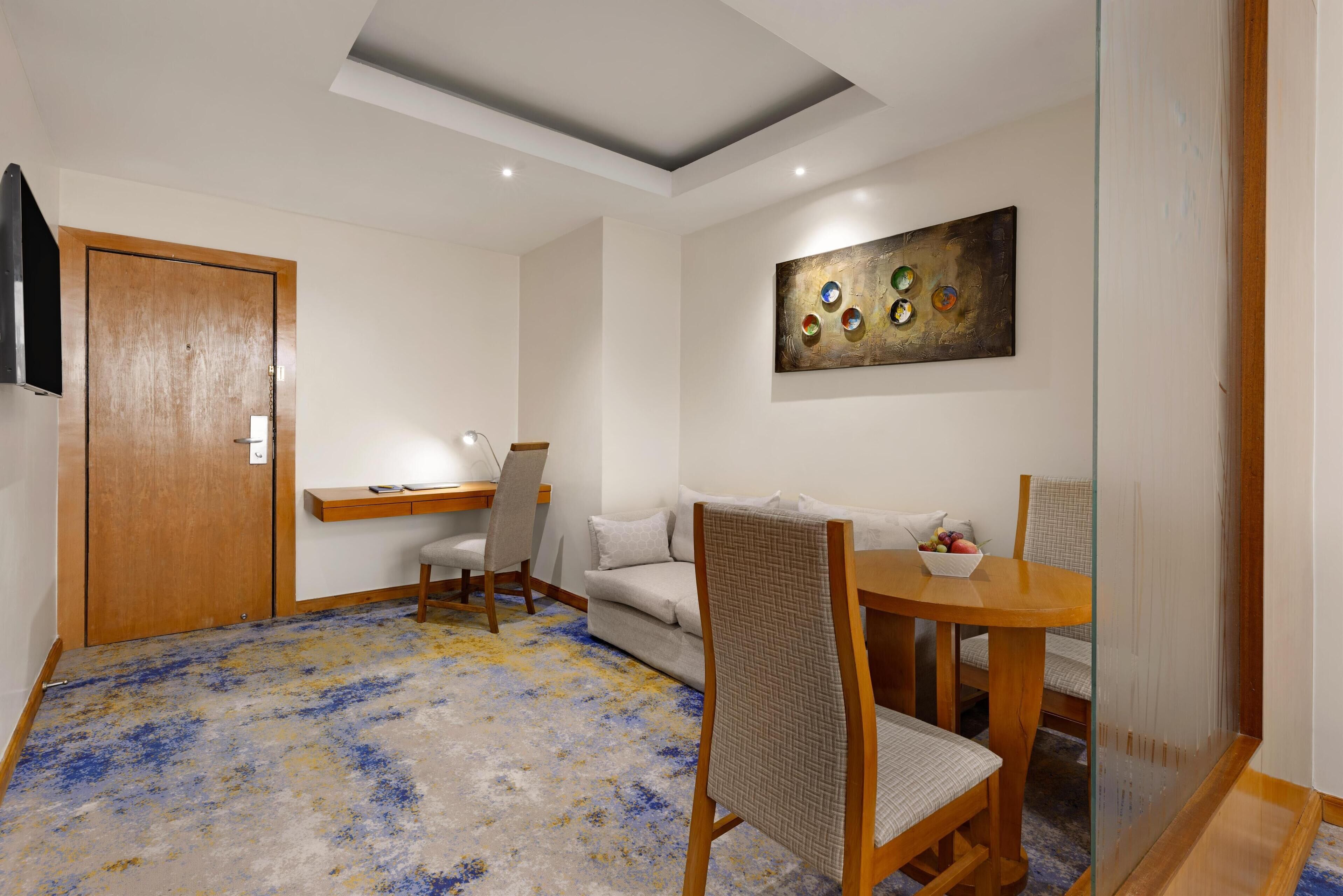 A modern room with a wooden door, a sofa, a dining table with chairs, and a ceiling light.