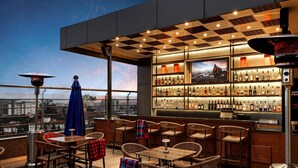 Eine Dachterrasse mit Blick auf die Stadt, Holztische und -stühle sowie eine gut sortierte Bar.