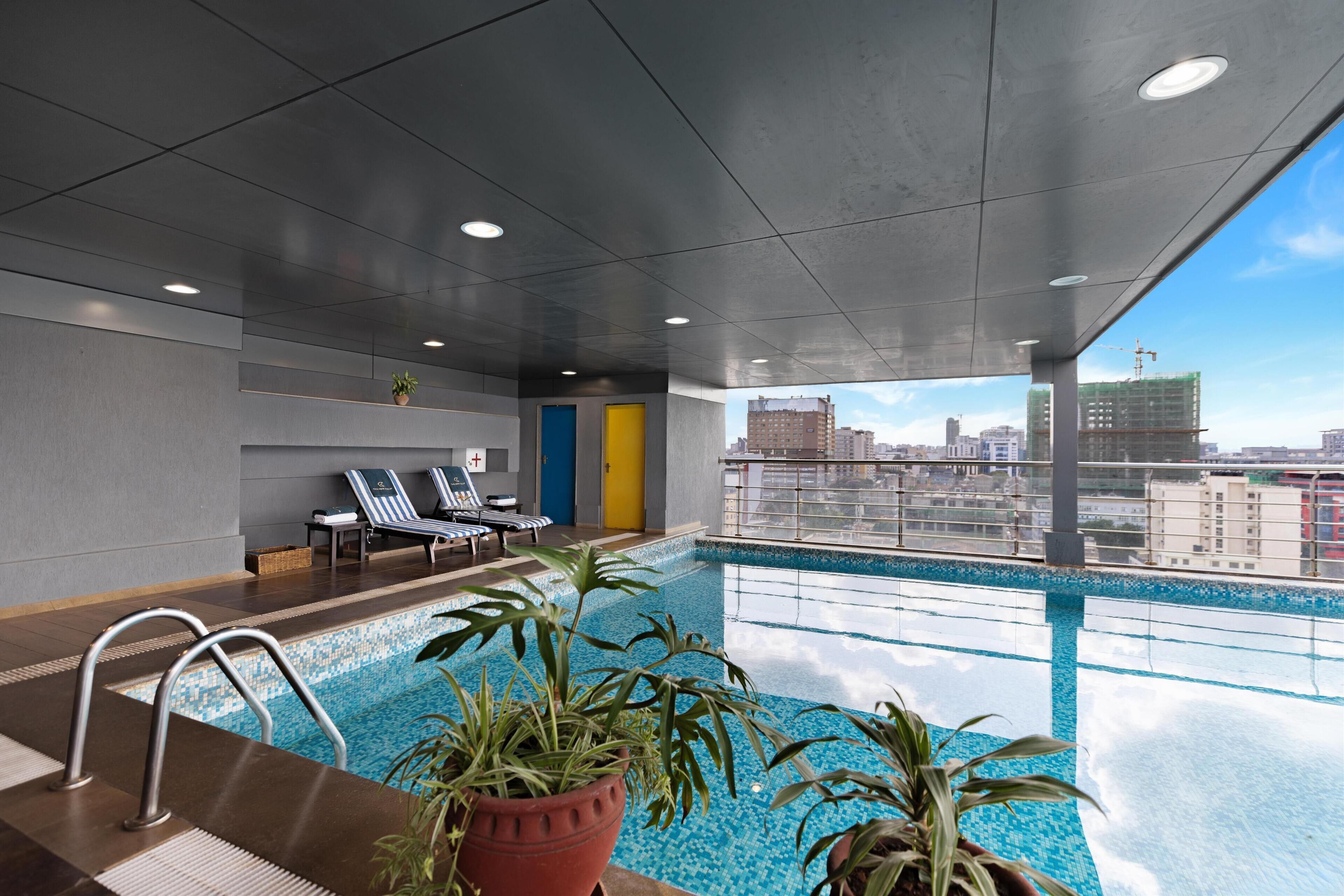 Un área de piscina interior moderna con sillones de descanso, una piscina y vistas a la ciudad.