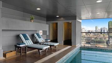 A modern indoor pool area with lounge chairs, a city view, and a tiled pool.