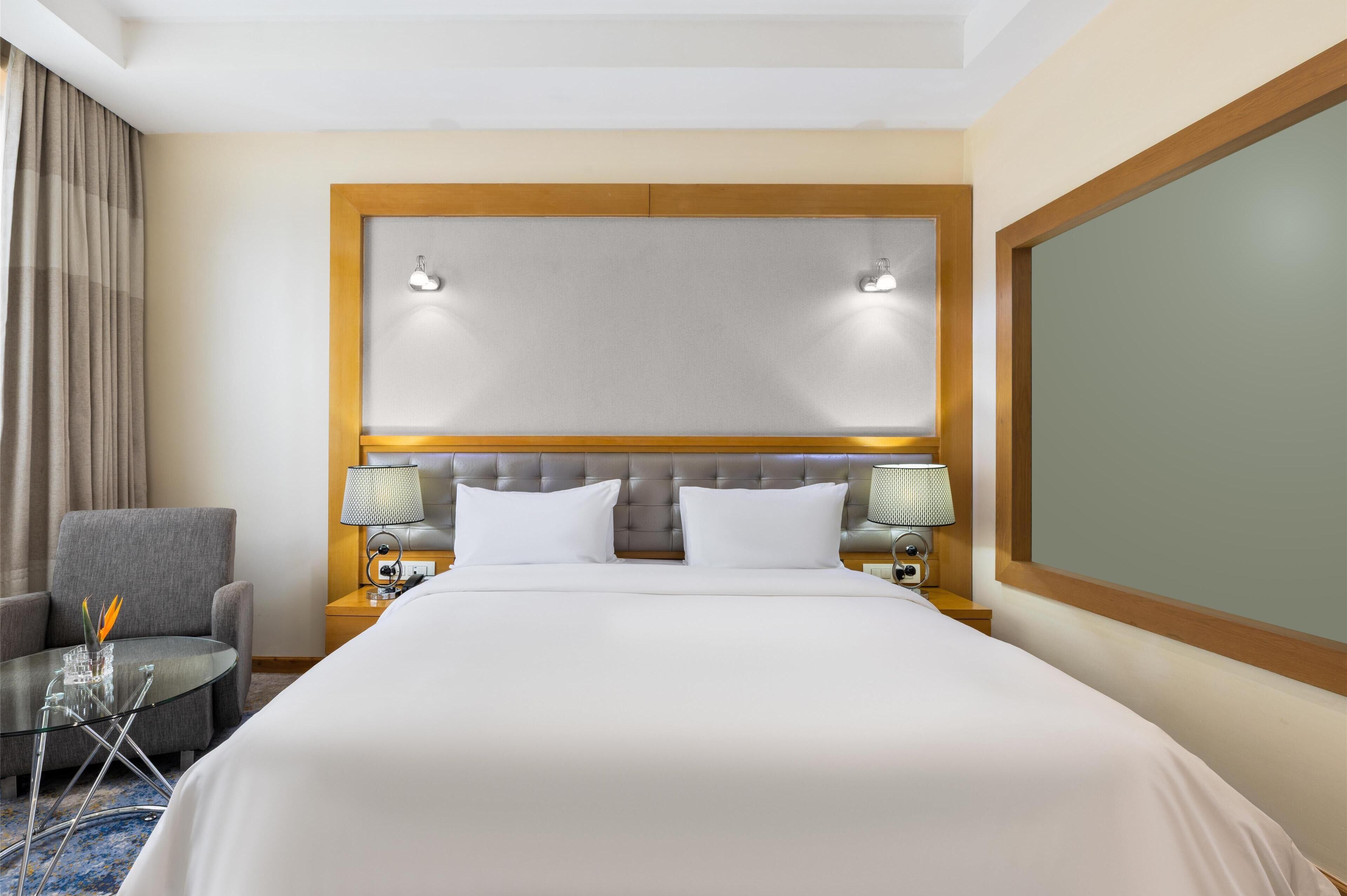 A hotel room with a large bed, two bedside lamps, a chair, and a small table with a lamp.