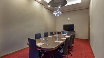 A conference room with a long table, chairs, water bottles, and a clock on the wall.