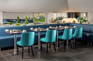 Een modern restaurant met blauwe zitplaatsen, uitzicht op groen en een eetgedeelte met tafels en stoelen.
