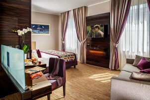 Camera d'albergo con un letto, una poltrona, una TV, una scrivania con un computer e una finestra con tende.