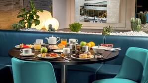 A breakfast table set with various food items and drinks, a coffee pot, and a view of a building with a sign reading "RomaTermini". - Gioberti Art Hotel (Rome)