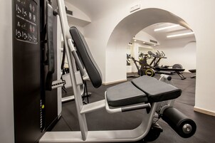 A gym with a leg curl/leg extension machine, a bench press, and an elliptical in the background.