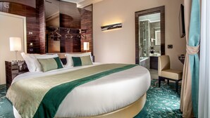 A large bed with a green and beige bedspread, a bedside table with a lamp, a chair, and a mirror in a hotel room. - Gioberti Art Hotel (Rome)