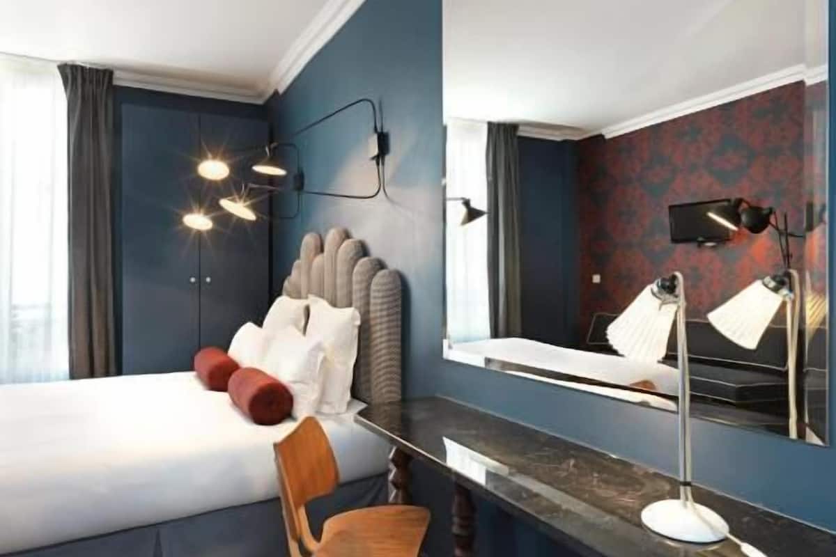 A hotel room with a bed, a desk, a chair, a desk lamp, a mirror, and a television.
