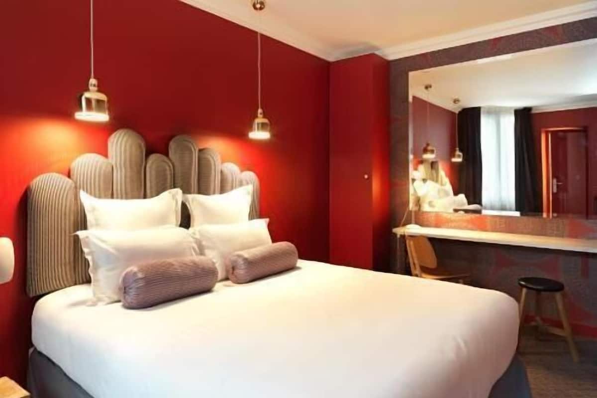 A hotel room with a large bed, a mirror, and a small stool.