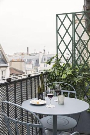 A balcony with a round table and chairs, a bottle of wine, and a glass of wine.