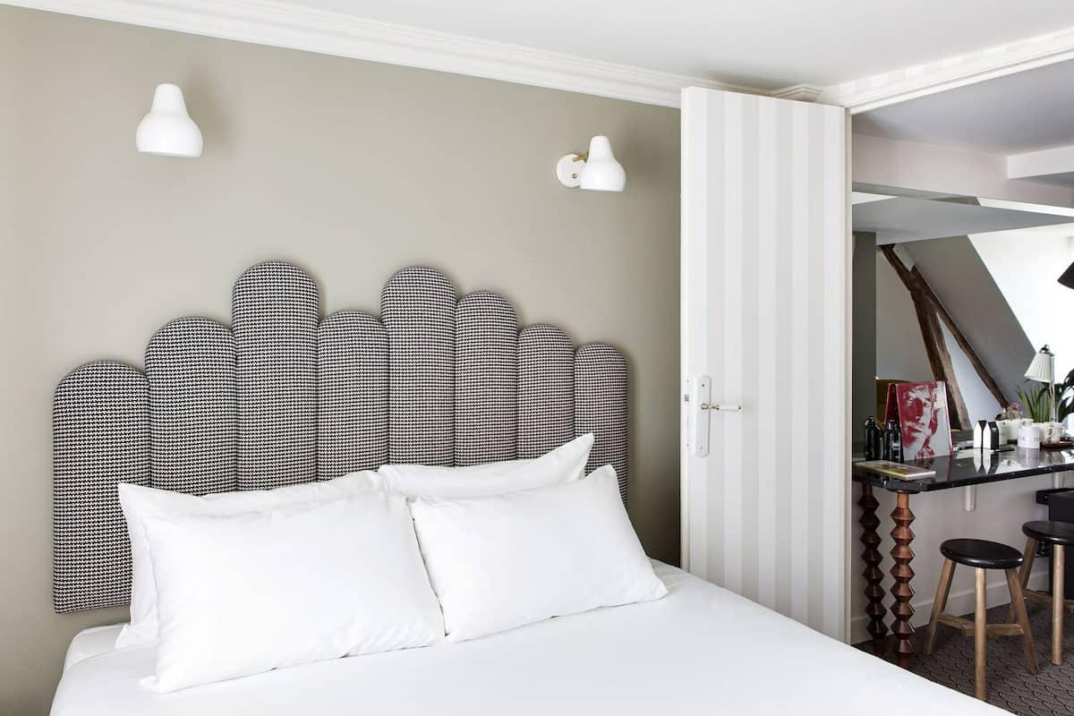 A bed with a patterned headboard, white pillows, and a desk with stools.