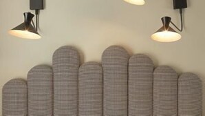 A wall-mounted lamp with a black base and a white shade, positioned above a textured wall panel. - Paradise Hotel (Paris)