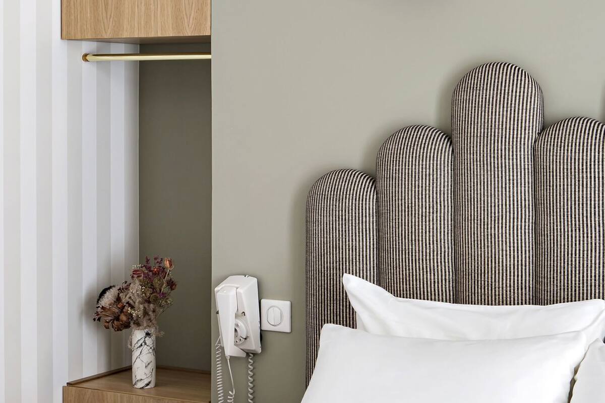 A hotel room with a bed, a bedside table with a phone, a lamp, and a wall-mounted shelf.