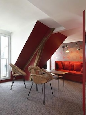 A room with a slanted ceiling, a red sofa, two wicker chairs, and a small table.