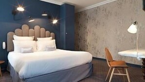 A hotel room with a bed, a desk, a chair, and a wall-mounted lamp. - Paradise Hotel (Paris)