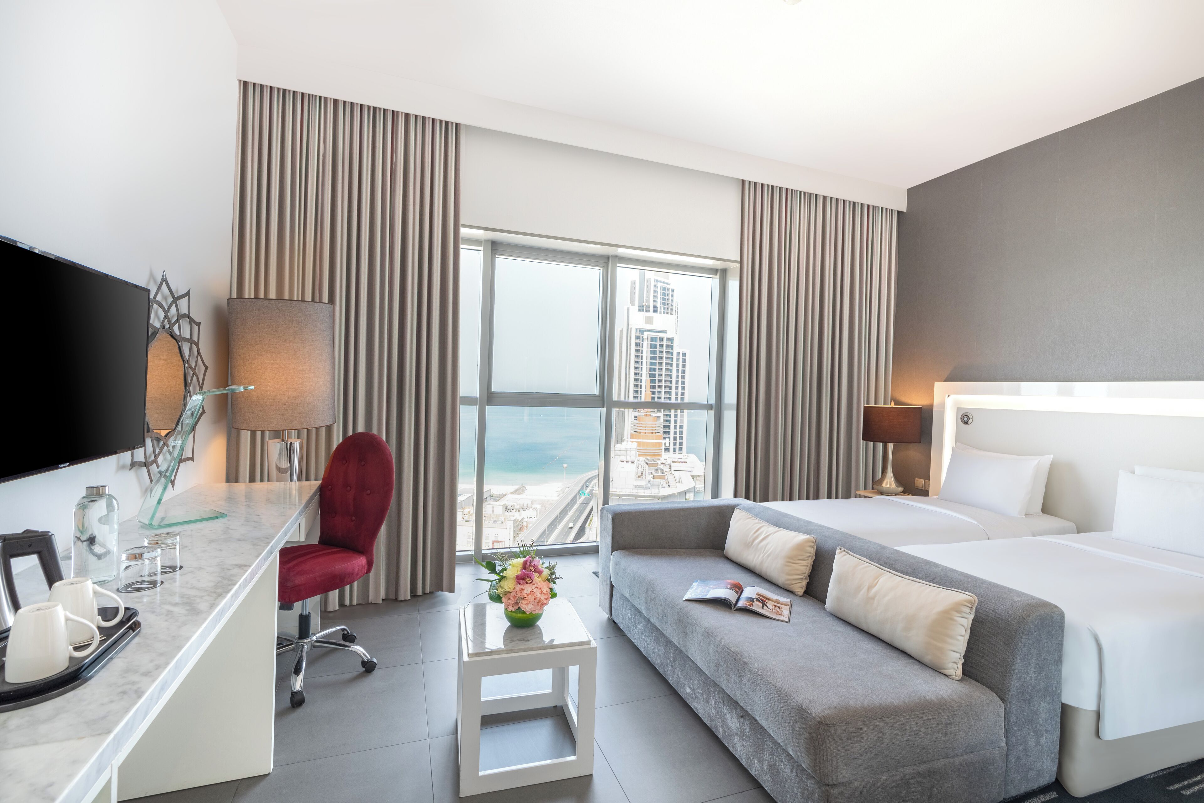 Een moderne hotelkamer met een groot bed, een bank, een bureau met een flatscreen-tv, een stoel en uitzicht op de stad.