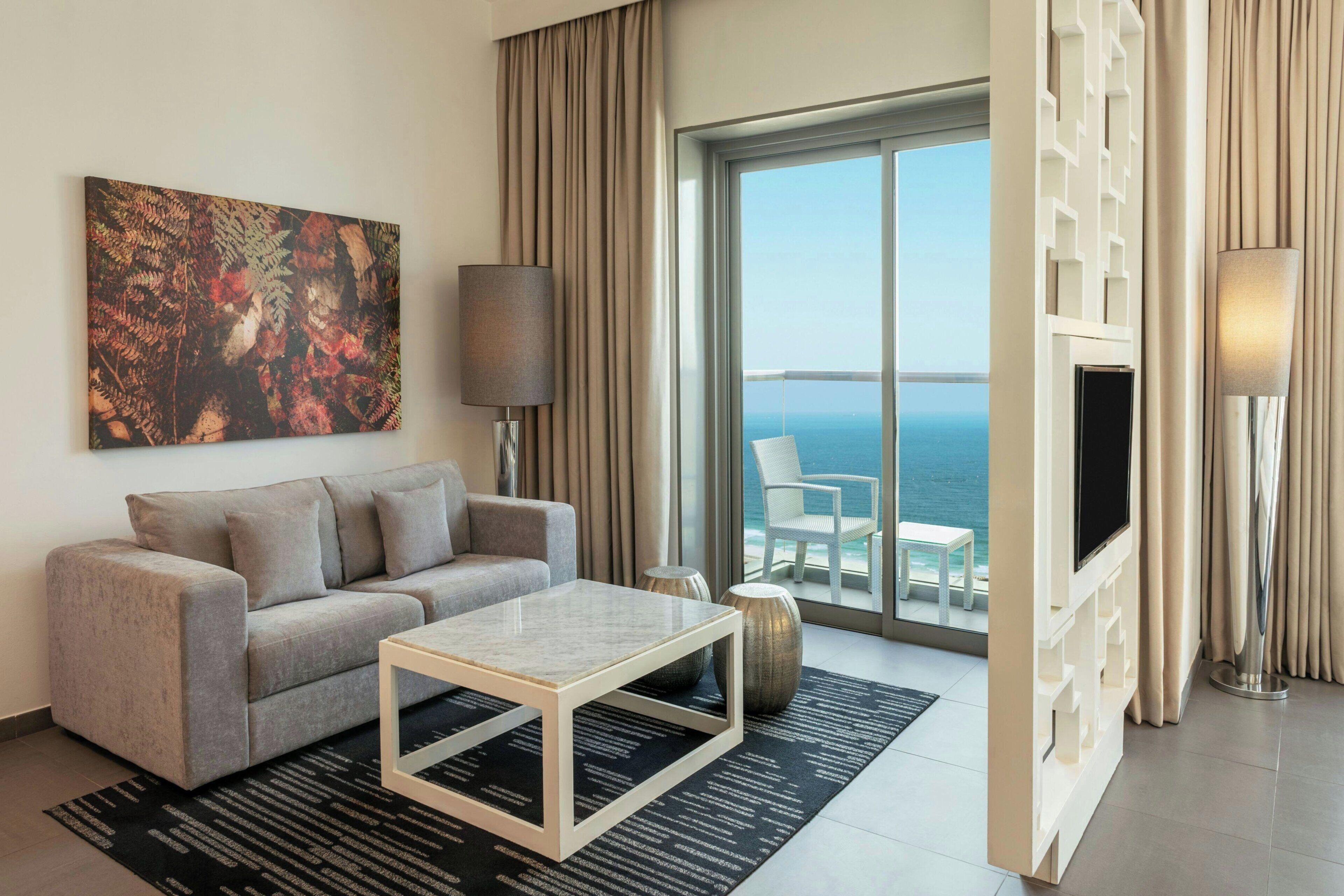 Een moderne hotelkamer met een bank, een bijzettafeltje, een televisie en een balkon met uitzicht op zee.