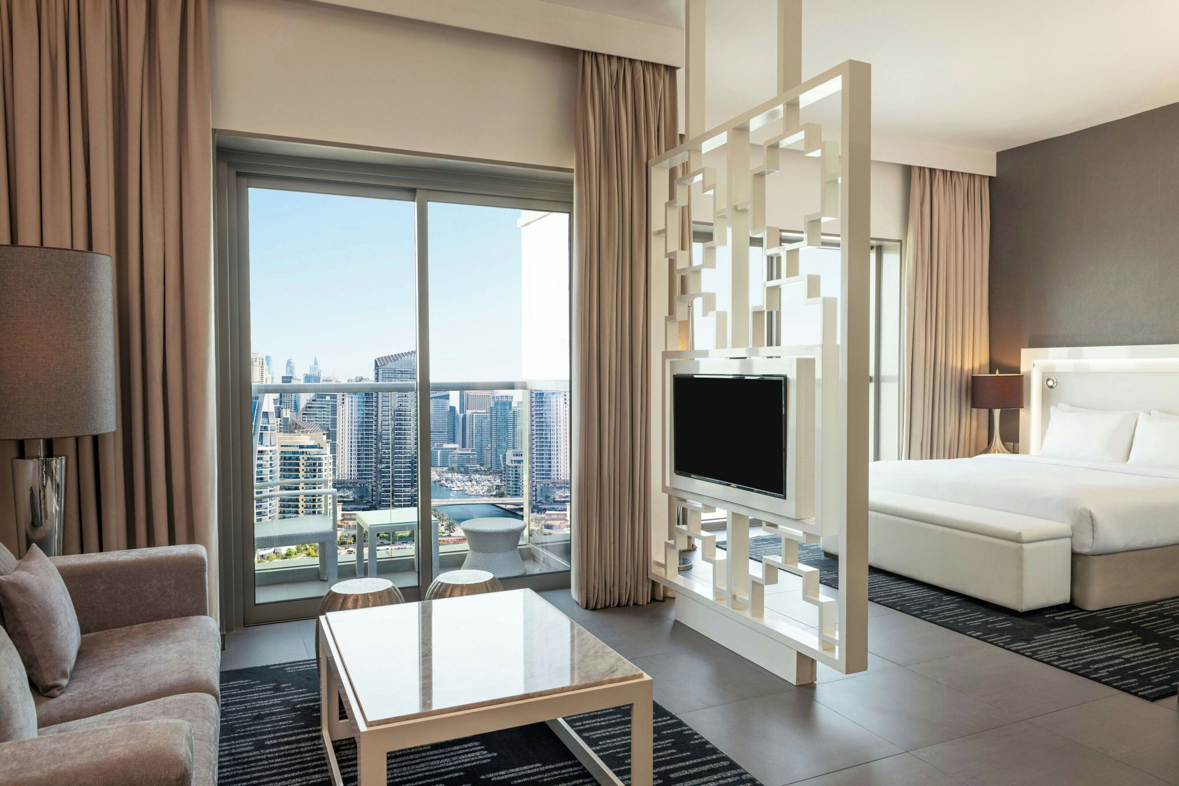 Une chambre d’hôtel moderne dotée d’une grande fenêtre, d’un téléviseur à écran plat, d’un canapé, d’une table basse et d’un lit.