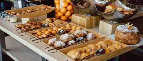 A buffet table with various pastries, fruits, and a large container of oranges.