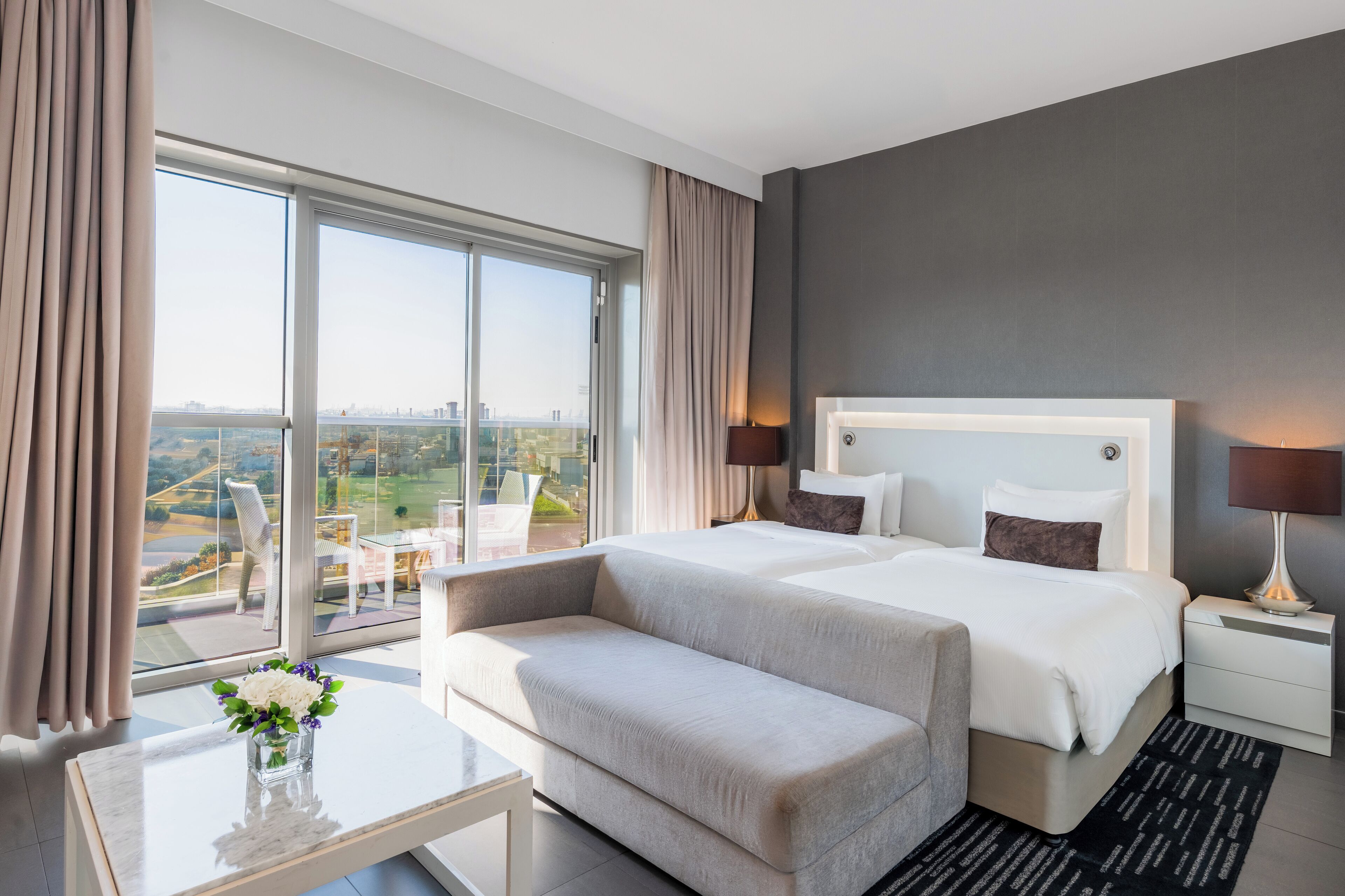 Une chambre d’hôtel avec un grand lit, un canapé, une petite table avec un vase et une vue sur la ville.