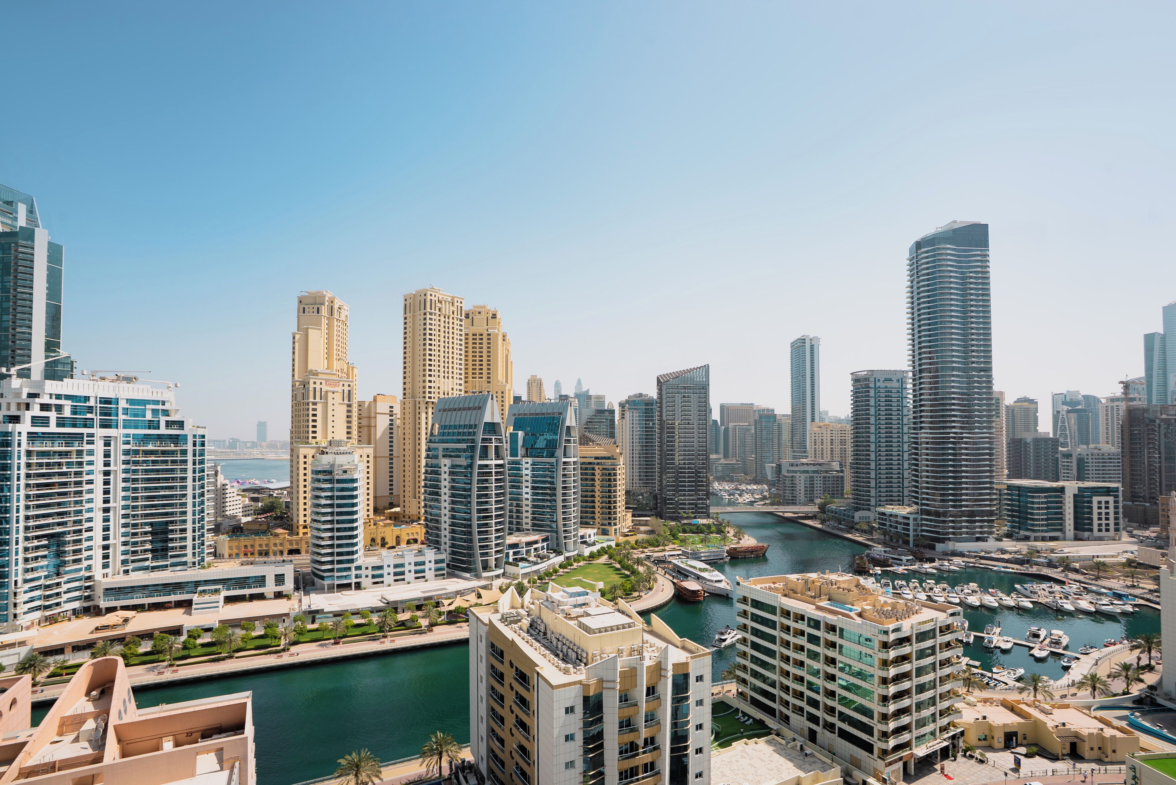 A high-rise urban area with modern architecture, a marina with boats, and a clear sky.