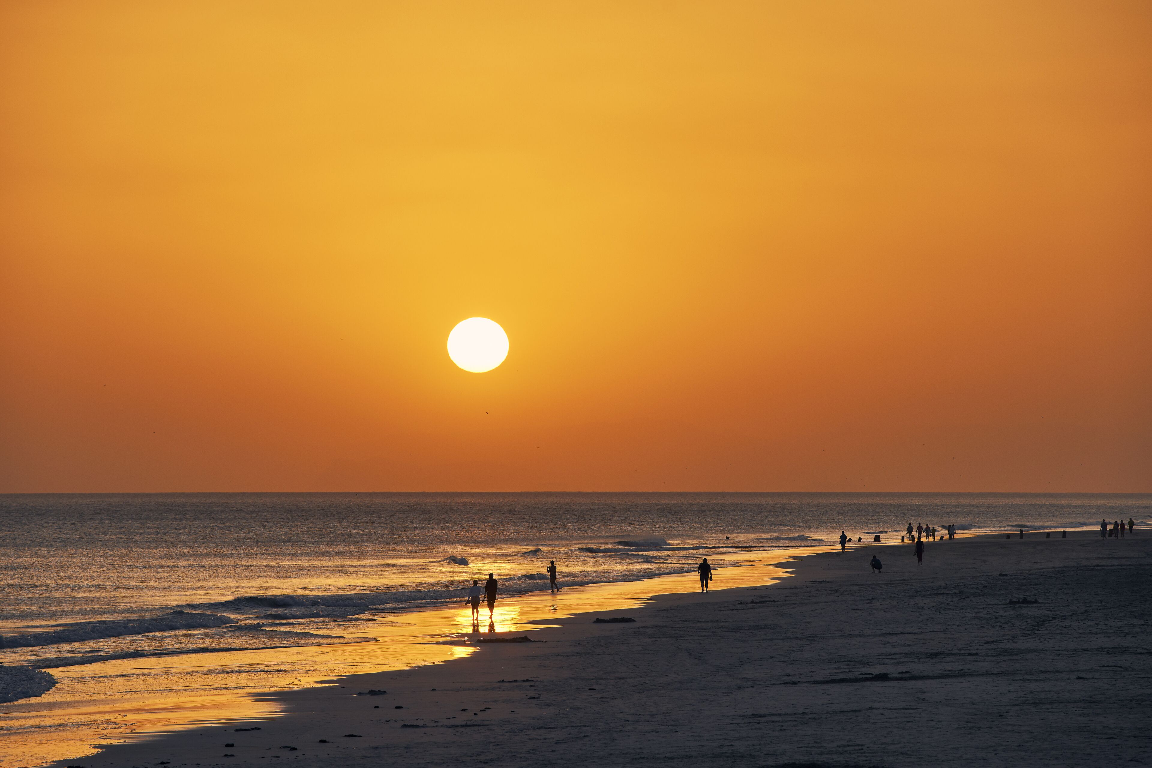 Una playa al atardecer con gente caminando por la orilla.