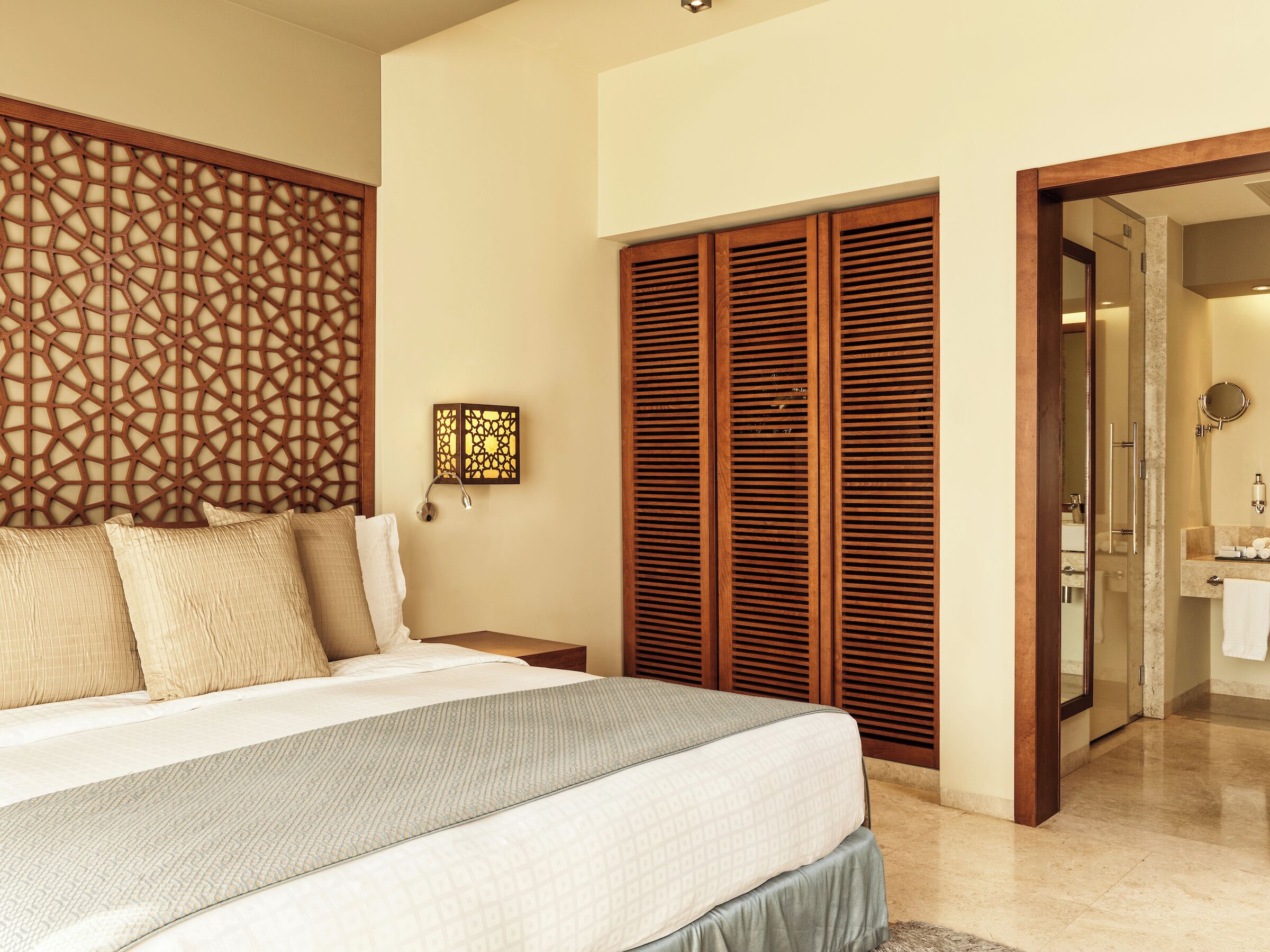 A bedroom with a large bed, wooden headboard, and a nightstand with a lamp.
