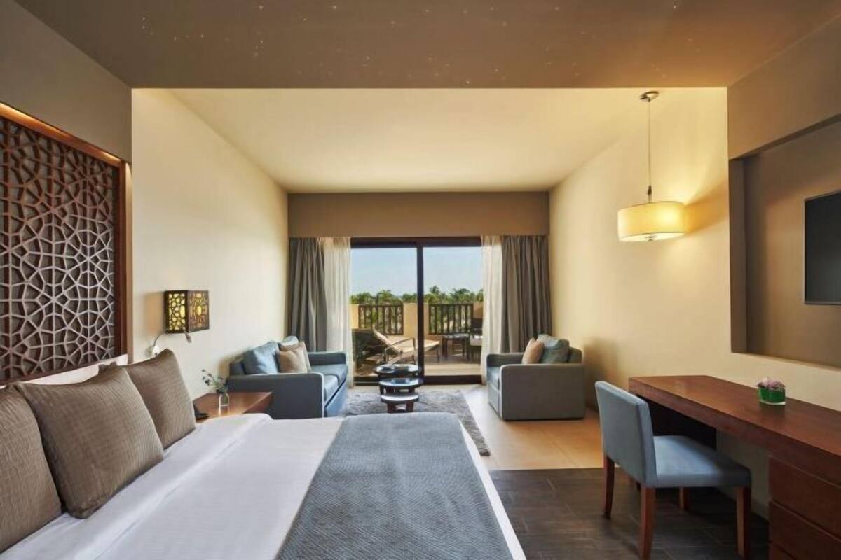 A hotel room with a bed, two sofas, a desk, and a balcony with a view.