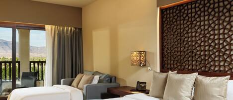 A hotel room with a large bed, a sofa, a desk, and a balcony with a view of the mountains.