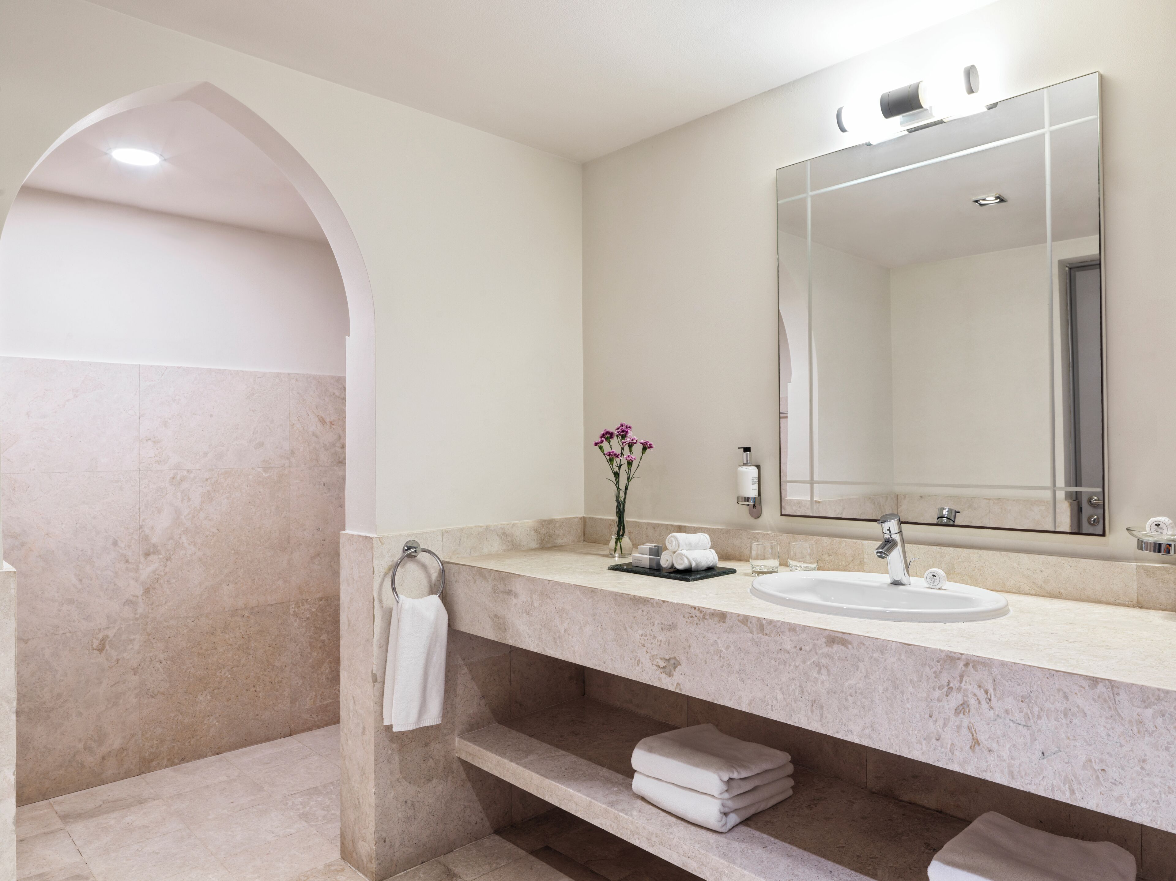 A modern bathroom with a marble sink, a large mirror, and a towel rack.