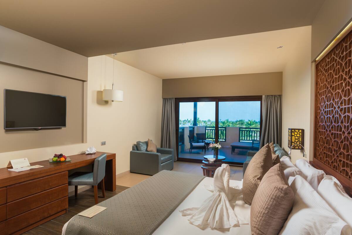 A hotel room with a bed, desk, and a TV. There is a balcony with a table and chairs.