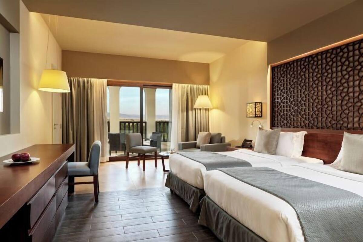 A hotel room with a large bed, a desk, a chair, and a view of the outdoors.