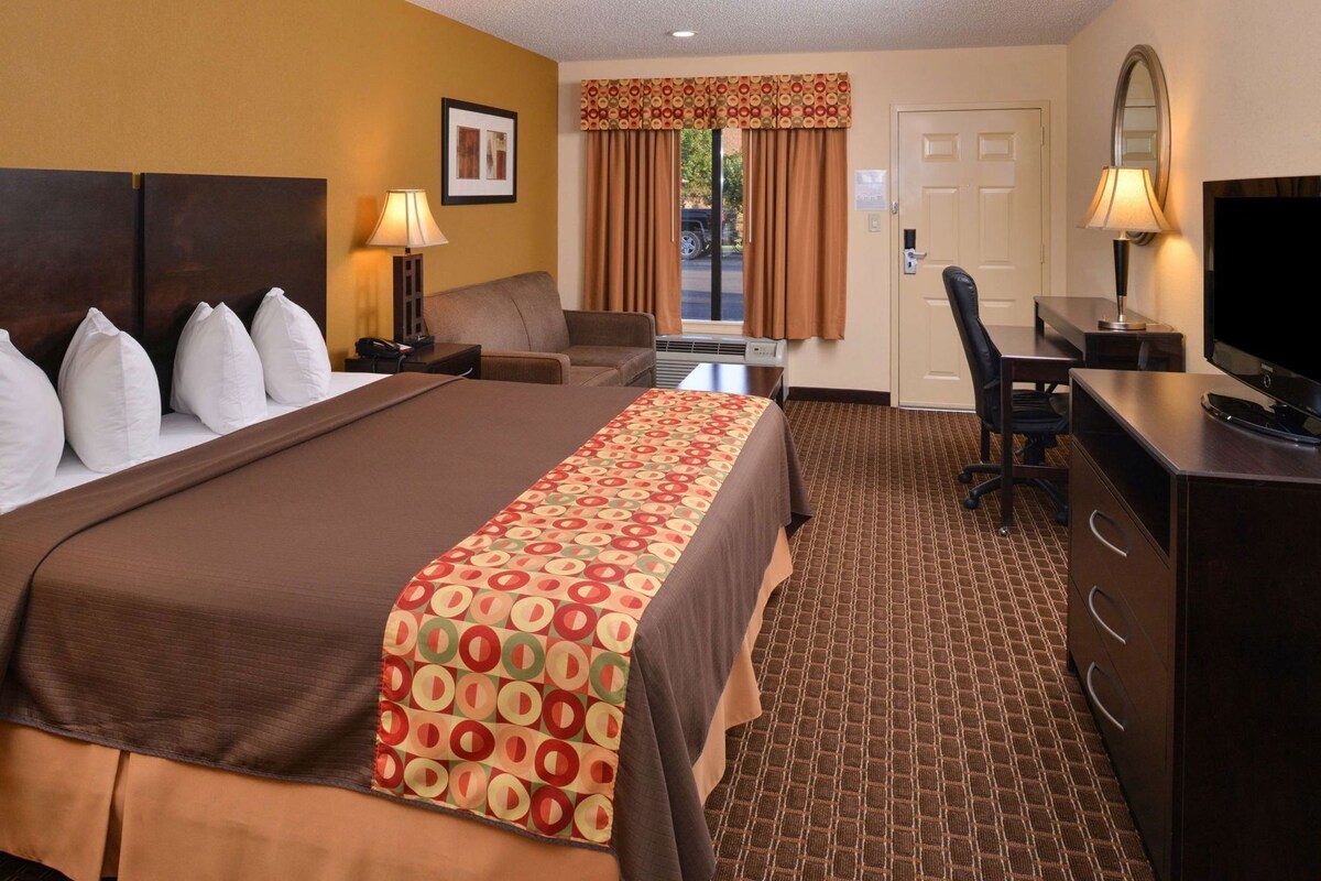 A hotel room with a large bed, a desk, a chair, a television, and a window with curtains.