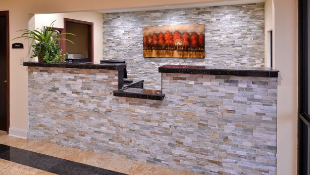 A reception area with a stone wall, a painting of autumn trees, and a potted plant. - Americas Best Value Inn Tupelo Barnes Crossing (Tupelo)