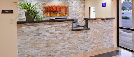 Un área de recepción con pared de piedra, planta en maceta y un cuadro.