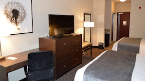 A hotel room with a desk, a television, a dresser, a bench, and two beds. - Best Western Plus Stevens County Inn (Hugoton)