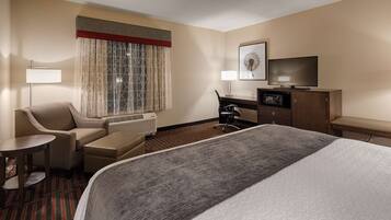 A hotel room with a bed, a desk, a chair, a TV, a microwave, and a window with curtains.